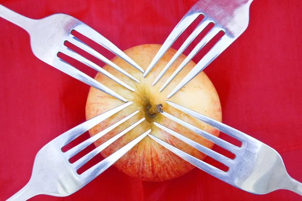 Red apple on red with four forks — Stock Photo, Image