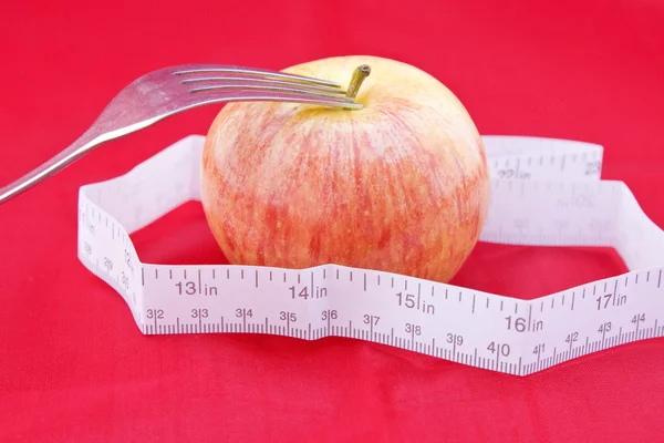 Golden-red apple with a meter and a fork on red — Stock Photo, Image