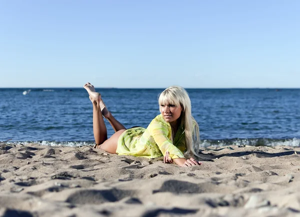 Sarı bir tunik sarışın kız dizlerinin üzerinde deniz kenarında yatıyor. — Stok fotoğraf