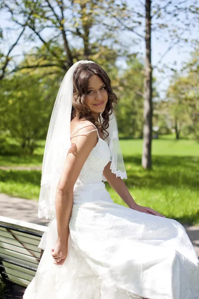 Beautiful young bride sitting on a park bench — Stock Photo, Image