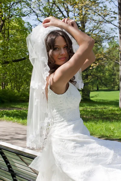 Beautiful young bride sitting on a park bench — Stock Photo, Image