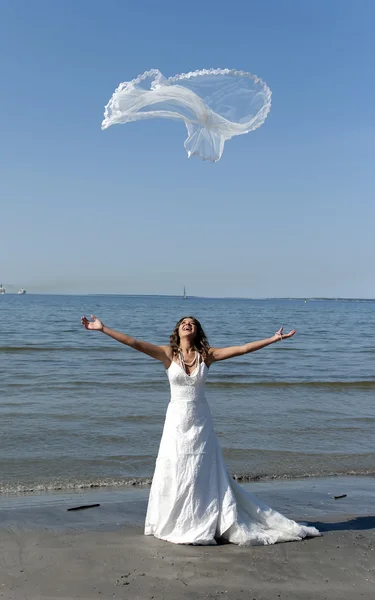 Beautiful young bride throwing the veil near the sea — Stock Photo, Image