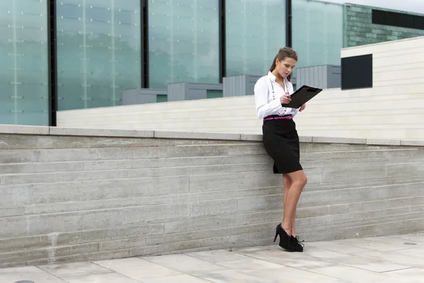 Zakelijke vrouw teken documenten op de achtergrond van een zakelijke gebouw — Stockfoto
