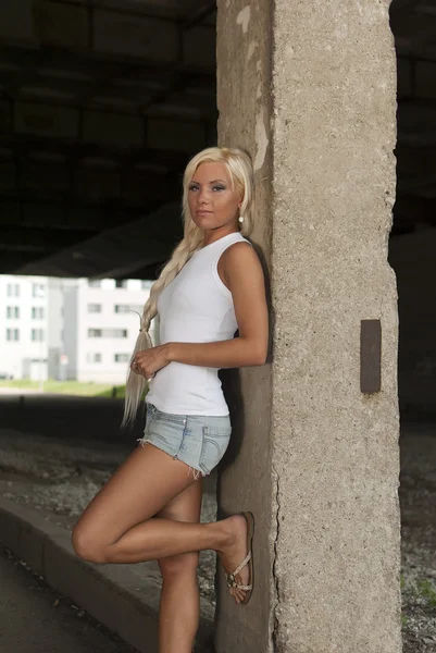 Athletic girl in denim shorts and white T-shirt standing at the pillar — Stock Photo, Image