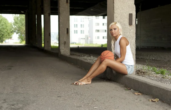 Prachtige blond meisje zit met basketbal op de straat — Stockfoto