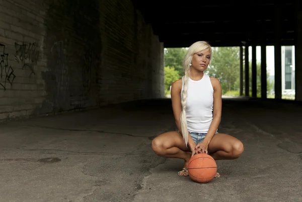 Prachtige blond meisje zit met basketbal op de straat — Stockfoto