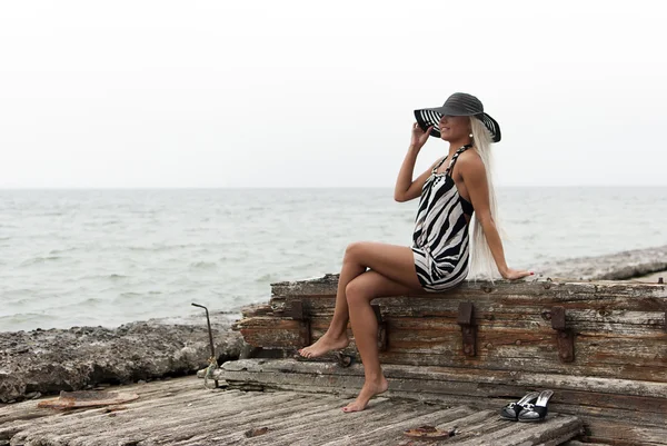 Chica del sombrero sentado en un barco roto en el mar — Stockfoto