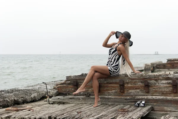 Chica en un sombrero sentado en un barco roto en el mar — Foto de Stock