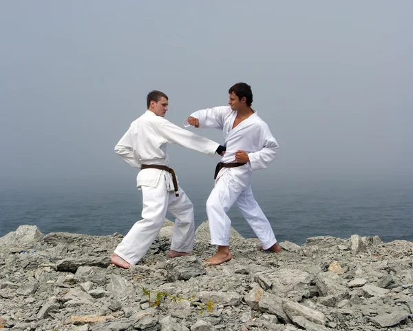 Two karateka fight on the banks of the misty sea — Stock Photo, Image