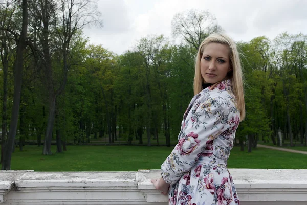 Blond flicka stående mot en bakgrund av park — Stockfoto