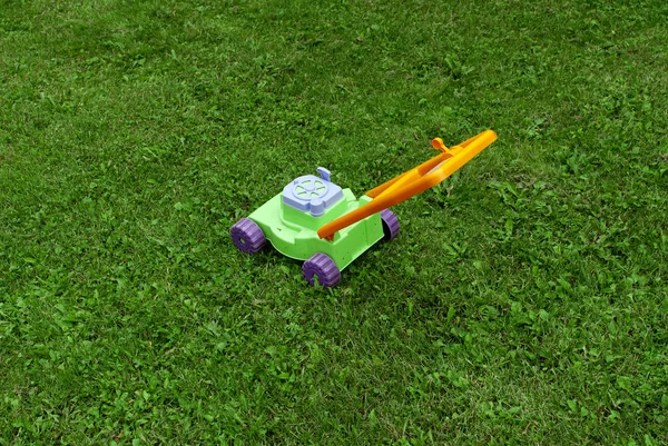 Cortador de grama de brinquedo infantil está na grama — Fotografia de Stock
