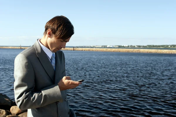 Homem de terno cinza marca o telefone contra o mar — Fotografia de Stock