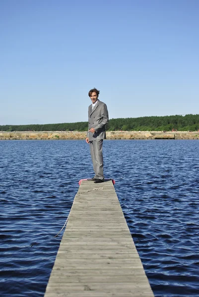 Άνθρωπος σε μια επιχείρηση της γκρι κοστούμι στέκεται σε μια προβλήτα κοντά στη θάλασσα — Φωτογραφία Αρχείου