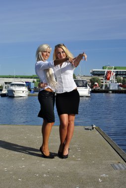 Two girls blonde stand on the pier and point a finger clipart