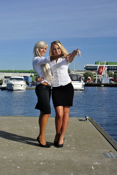 Two girls blonde stand on the pier and point a finger — Stock Photo, Image
