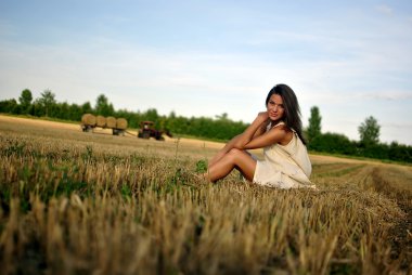 kırsal kesimde bir alan üzerinde oturan Ulusal elbiseli güzel kız