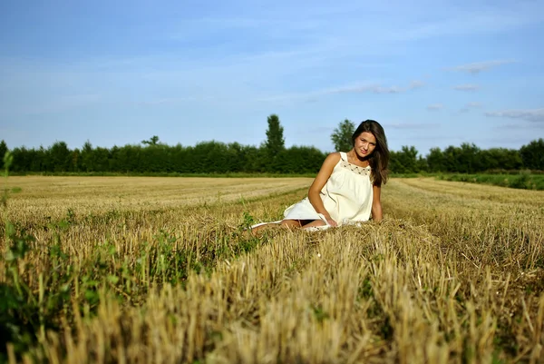 Leuk meisje in nationale klederdracht zittend op een veld in plattelandsgebieden — Stockfoto