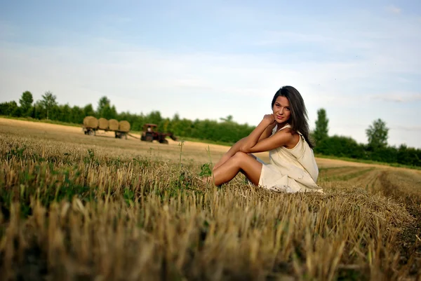 Menina agradável em vestido nacional sentado em um campo em áreas rurais — Fotografia de Stock
