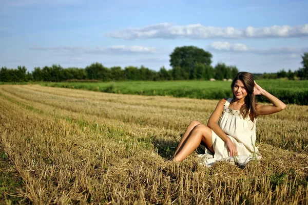 Trevlig tjej i nationella klänning sitter på ett fält i landsbygdsområden — Stockfoto