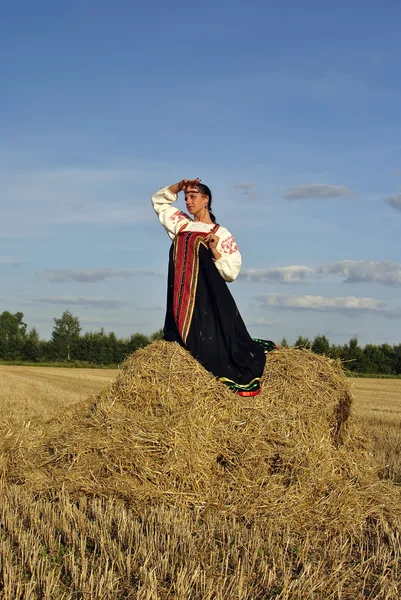 Κοπέλα με παραδοσιακή ρωσική φορεσιά που κάθεται σε μια θυμωνιά χόρτου — Φωτογραφία Αρχείου