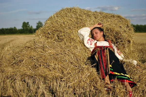 Fille en costume traditionnel russe reposant sur une meule de foin — Photo