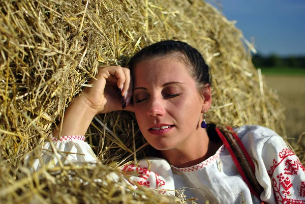 Flicka i traditionell rysk dräkt vilar på en höstack — Stockfoto
