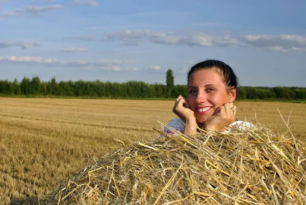 Mädchen in traditioneller russischer Tracht liegt auf einem Heuhaufen und lächelt — Stockfoto