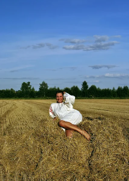 在传统的俄罗斯服装坐在干草堆上，微笑的女孩 — 图库照片