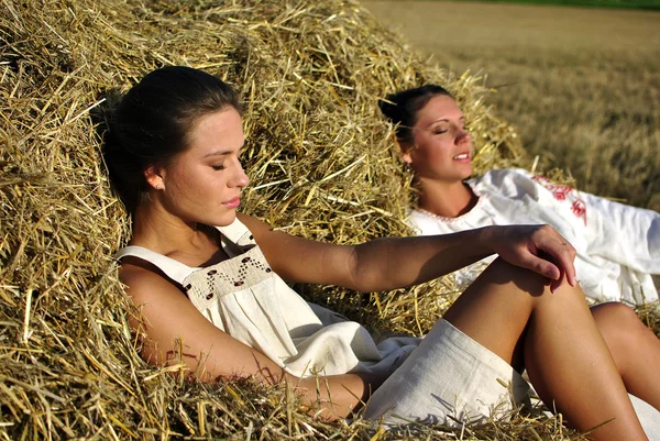 Two girls in traditional Russian costume resting on a haystack — Stock Photo, Image