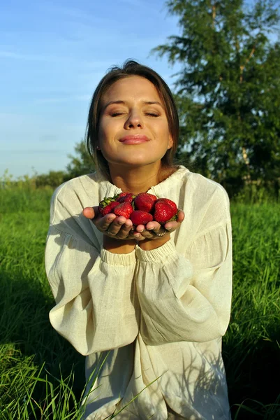Girl in a linen shirt, holding a strawberry in hand — Stock Photo, Image