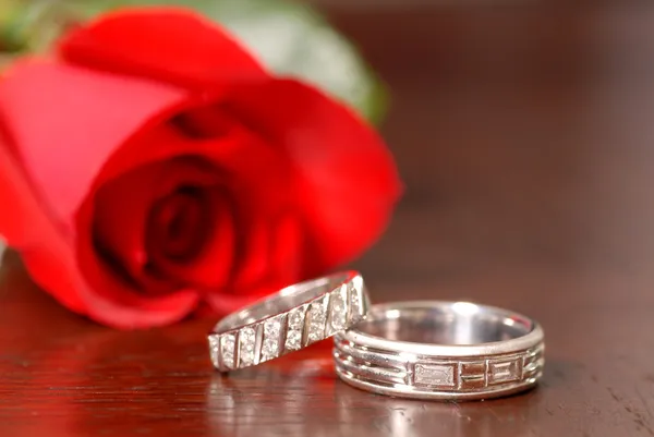 Dva snubní prsteny s červenou růží na stůl — Stock fotografie