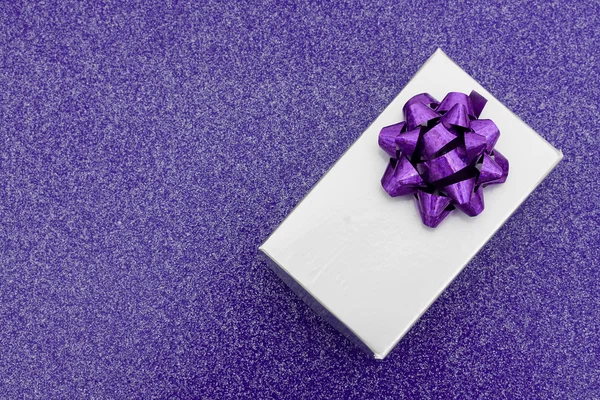 Серебряный подарок с луком на фиолетовом фоне — стоковое фото