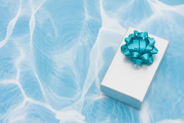 Un regalo d'argento con fiocco su sfondo acqua — Foto Stock