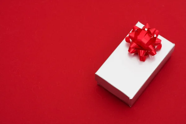 Серебряный подарок с луком на красном фоне — стоковое фото