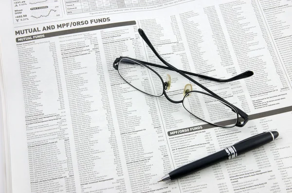 Óculos, caneta e fundos mútuos em jornal — Fotografia de Stock