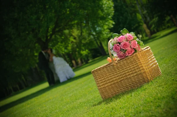 Bröllop ros bukett på en korg och nygift par i naturen — Stockfoto