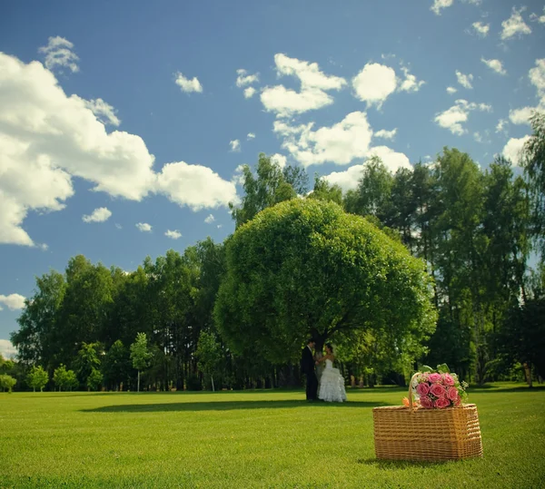 Hochzeit Rosenstrauß auf einem Korb und Brautpaar in der Natur — Stockfoto
