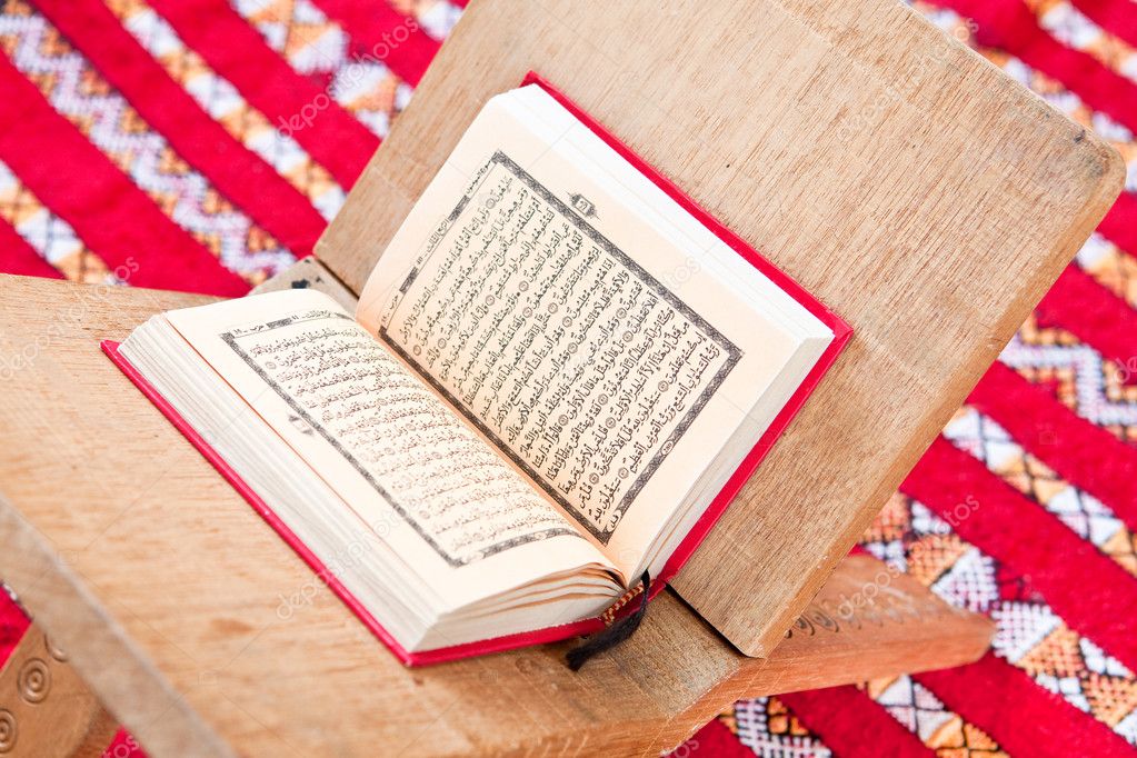 Warsh quran open on a wooden stand on a red Moroccan rug