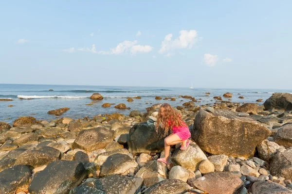 Sevimli küçük kız tarama kayaların üzerinde kayalık sahil. — Stok fotoğraf