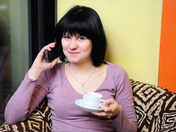 Flicka håller kaffe och använder sin mobiltelefon — Stockfoto