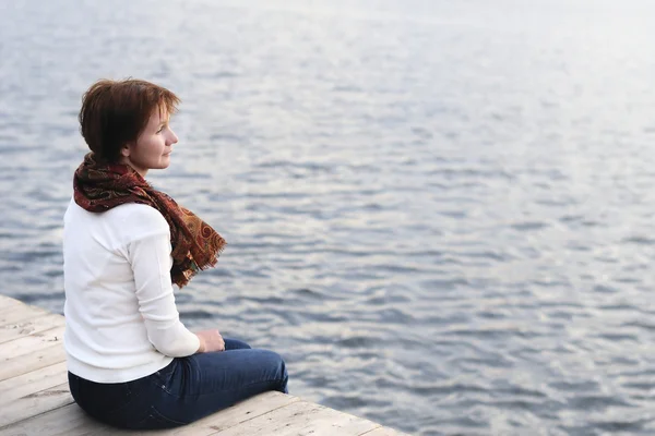 Uma mulher está sentada junto à água. — Fotografia de Stock