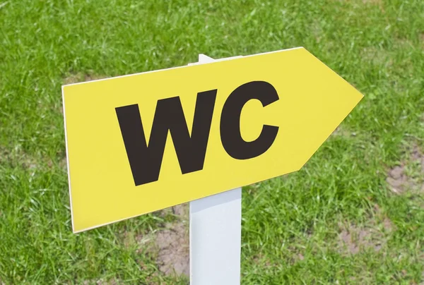 WC sign pointing direction on a green grass — Stock Photo, Image