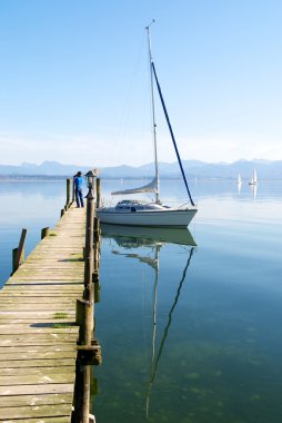 Sailing boat and reflection in peaceful lake pier clipart