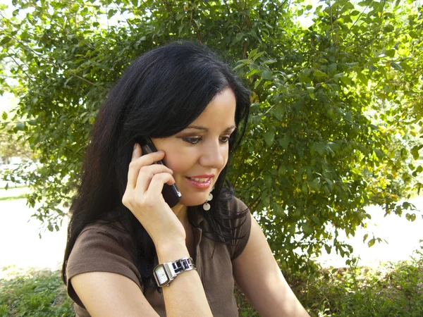 Piękna młoda brunetka kobieta rozmawia z jej telefonu komórkowego w ogrodzie — Zdjęcie stockowe