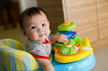 6 month old Asian baby girl plays sitting in a walker clipart