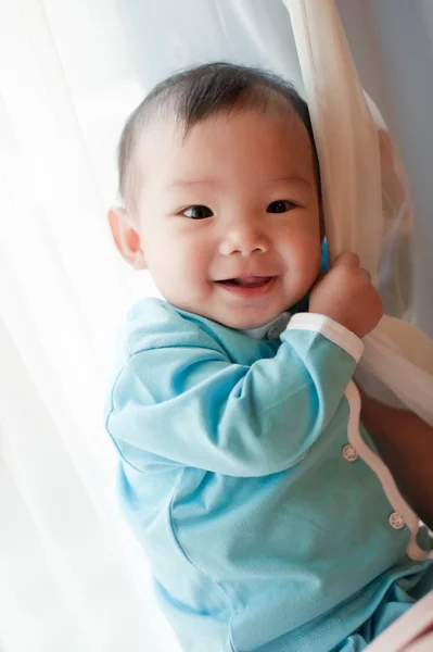 7 month old Asian baby girl smiling and holding on to a curtain — Stock Photo, Image