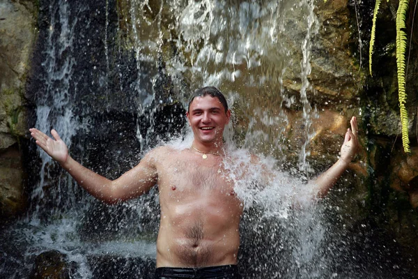 Молодой человек под водопадом — стоковое фото