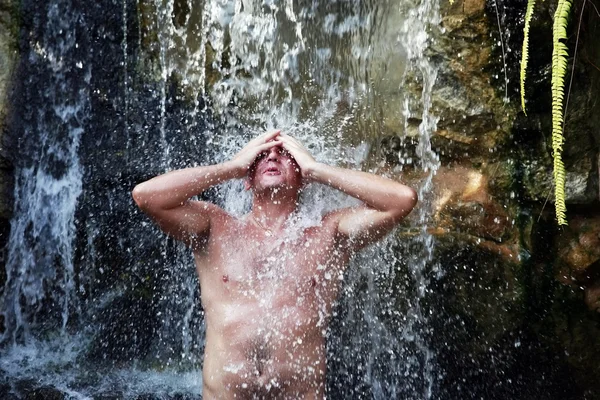 Der junge Mann unter einem Wasserfall — Stockfoto