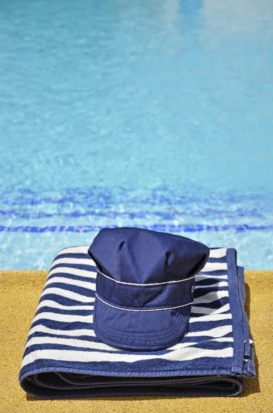 Rybářská čepice a pruhovaný ručník v bazénu — Stock fotografie