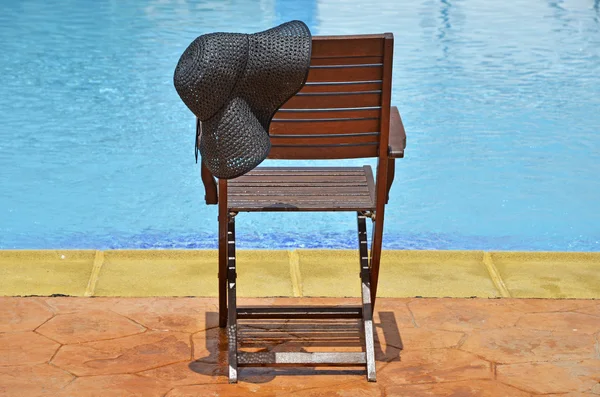 Chapéu e cadeira de madeira à beira da piscina — Fotografia de Stock